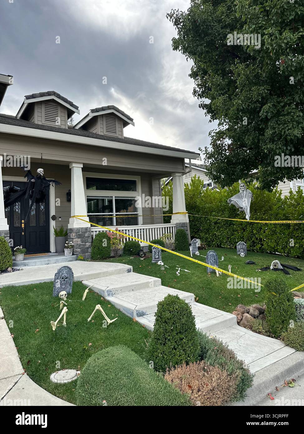 Suburban house front yard transformed into a Halloween scene with skeletons, gravestones, caution tape, and ghost decorations. Stock Photo