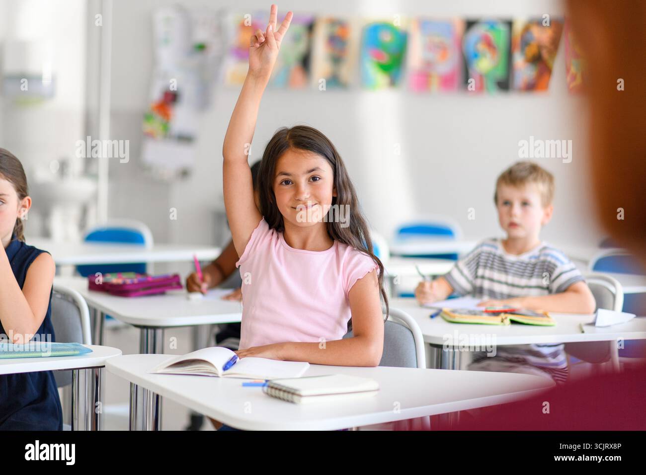 School girl sitting at the desk in classroom on the lesson, raising ...