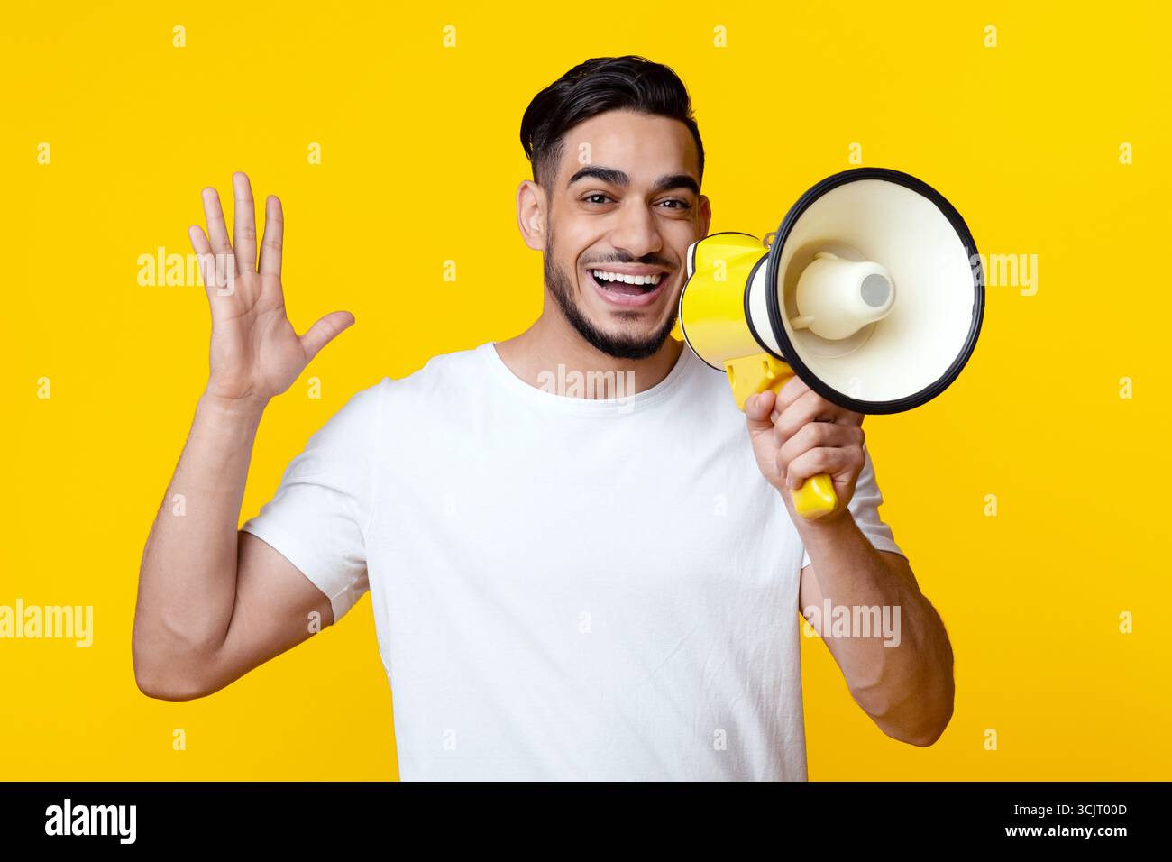 Excited arab guy speaking loud, using megaphone on yellow Stock Photo