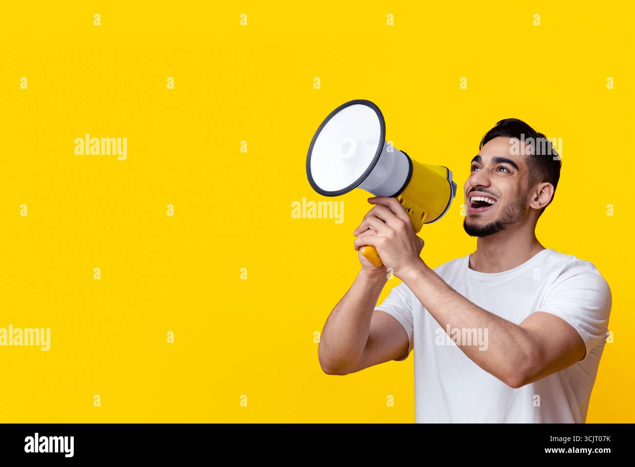 Excited arab guy speaking loud, using megaphone on yellow Stock Photo
