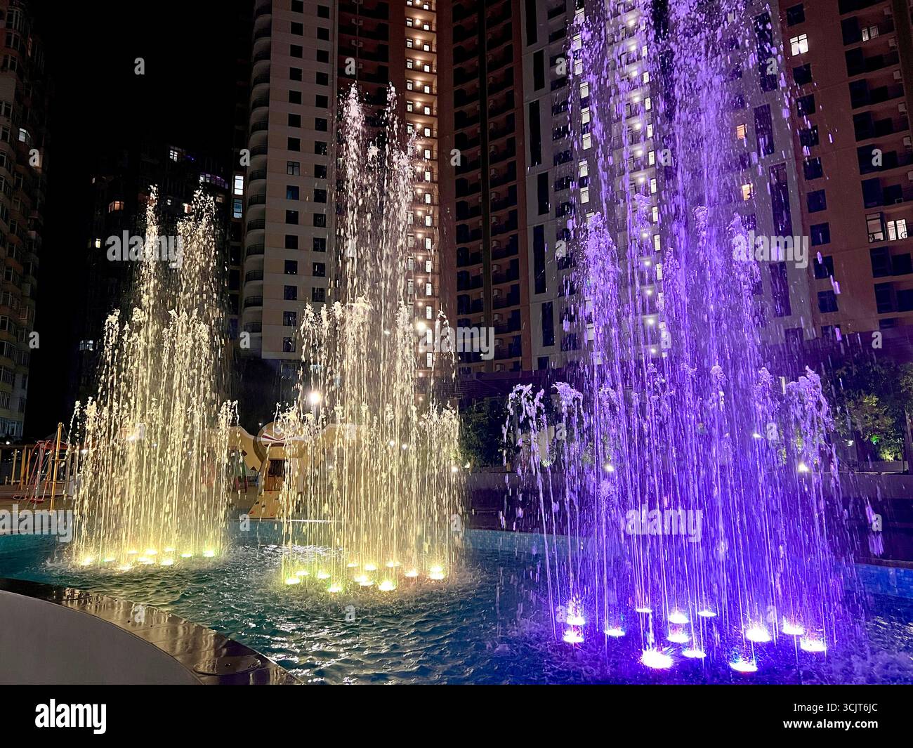 singing fountain with purple and yellow colored lighting in the middle of the city area - Smartphone Captured Stock Image