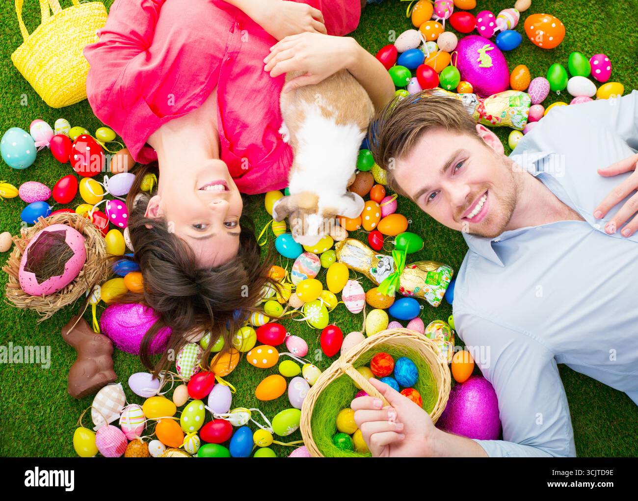 couple lying with an Easter bunny between many colourful Easter eggs on a meadow Stock Photo