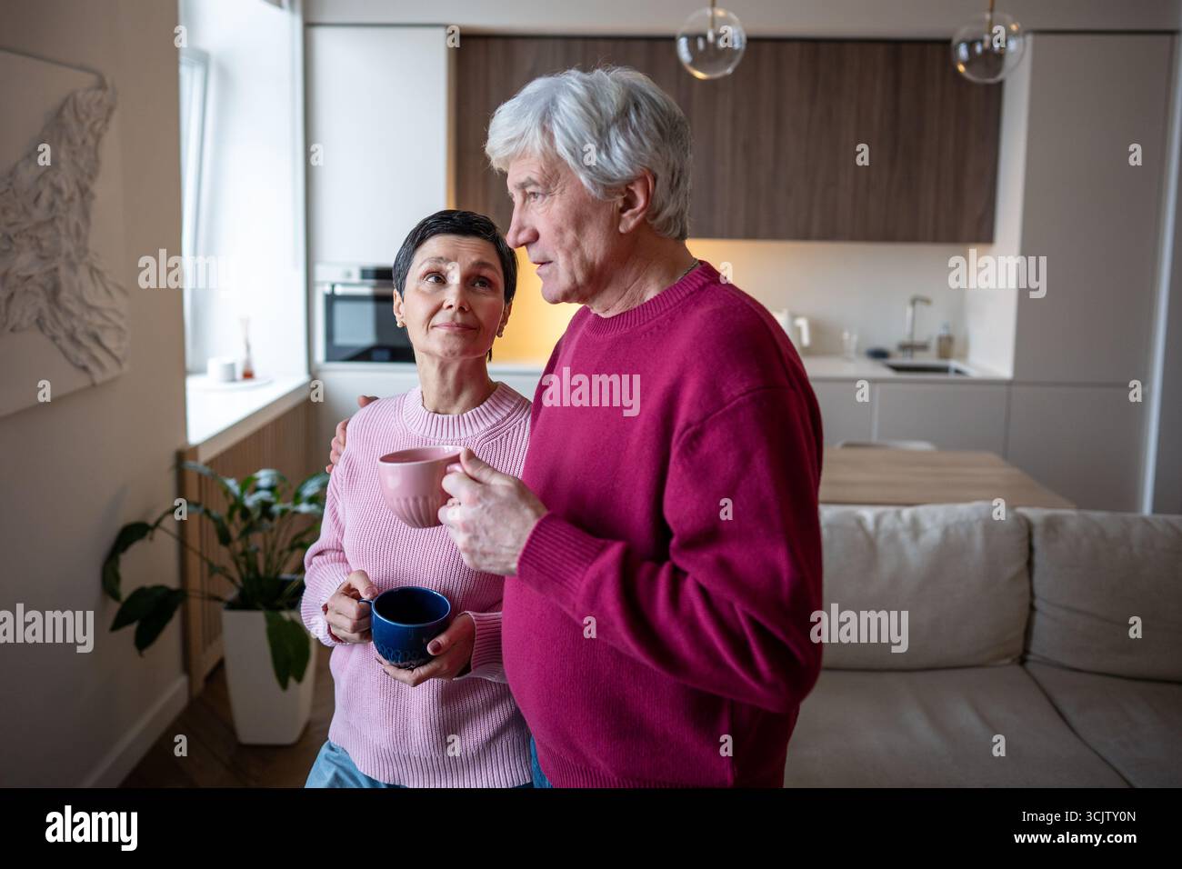 Calm elderly couple talking and drinking tea coffee at home wife looking at husband with loving eyes Stock Photo