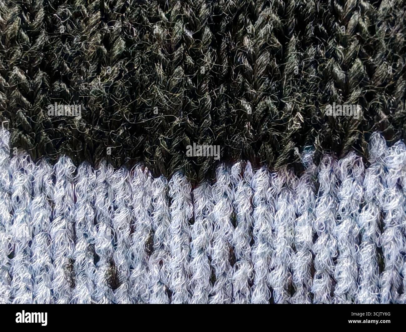Detailed macro shot of a two-tone knitted fabric, featuring a distinct division between a dark, textured section and a lighter, fuzzy one. Stock Photo