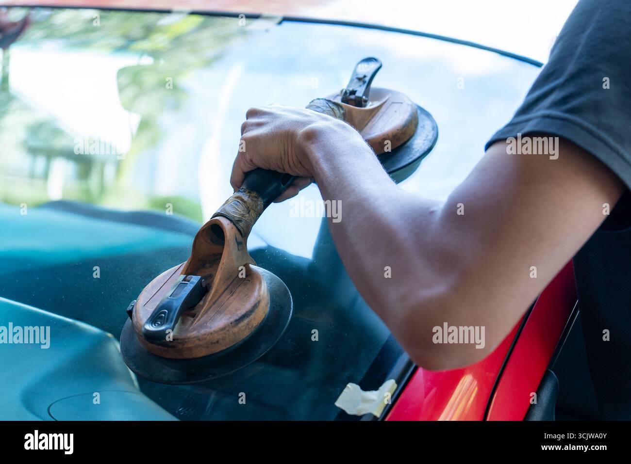 Hand using a heavy-duty suction cup tool on a car's windshield. Auto glass repair, windshield installation concept. Stock Photo