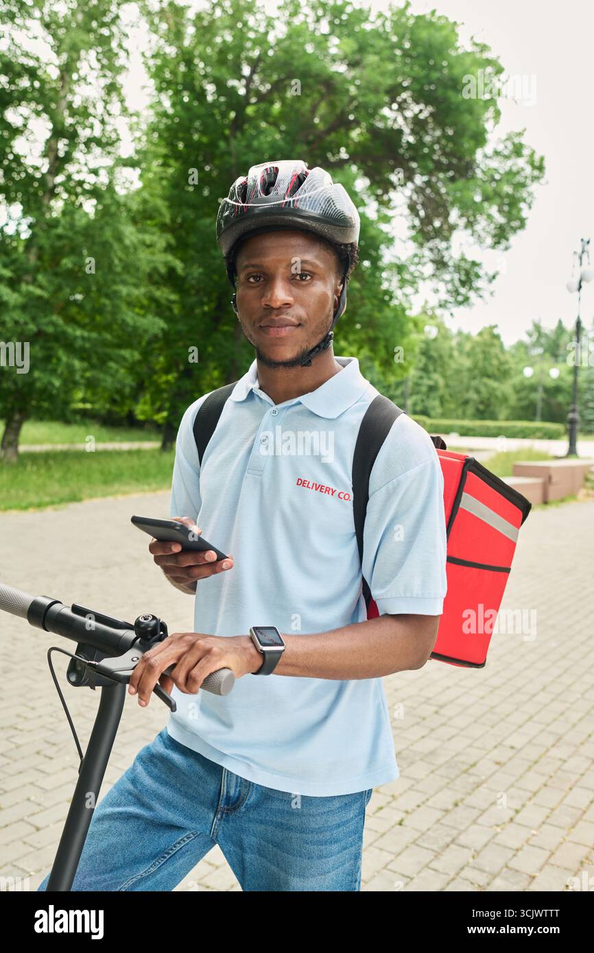 Black Man Using Smartphone While Standing with Electric Scooter Stock Photo