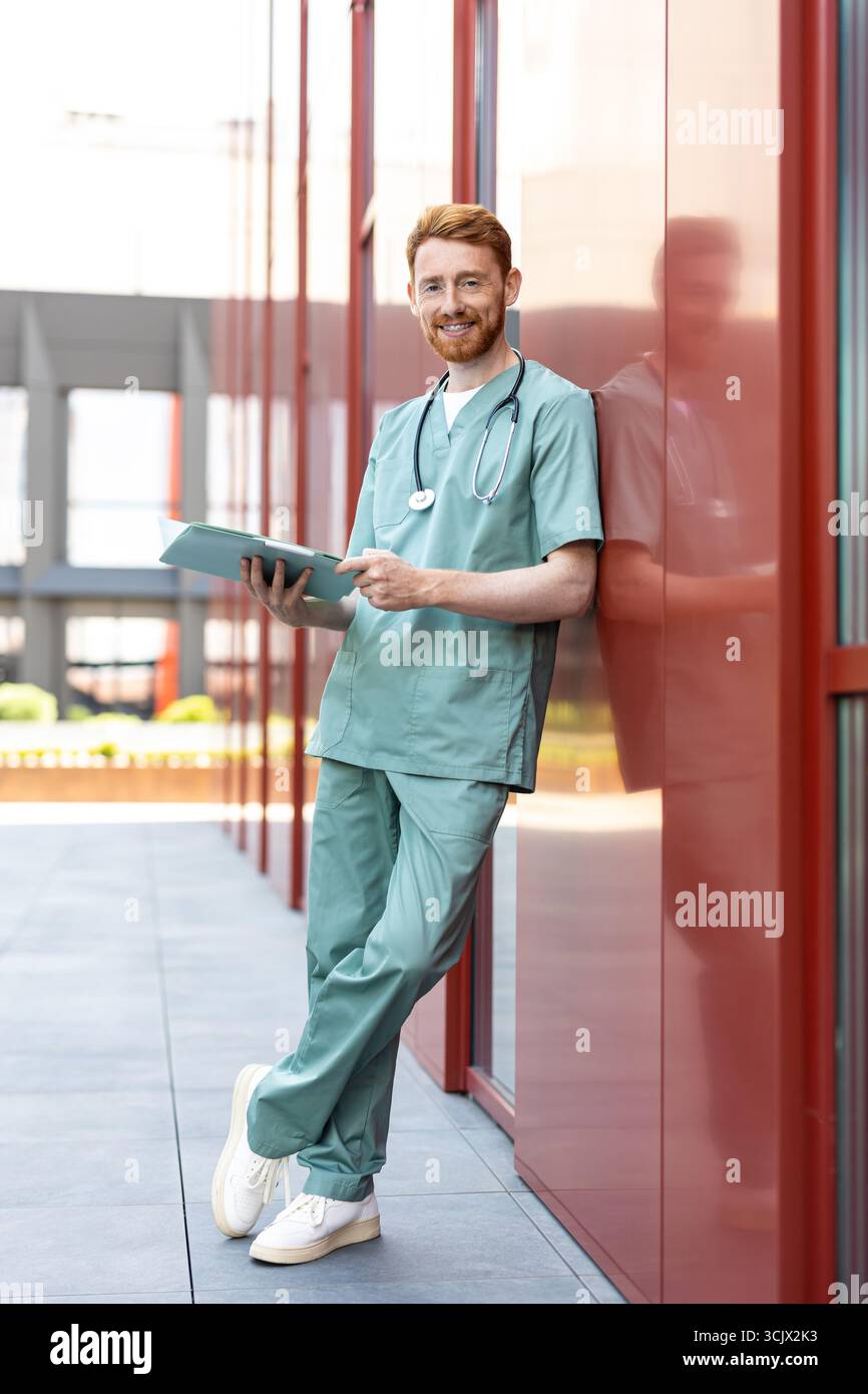 Man physician reading open folder leaning near clinic wall Stock Photo