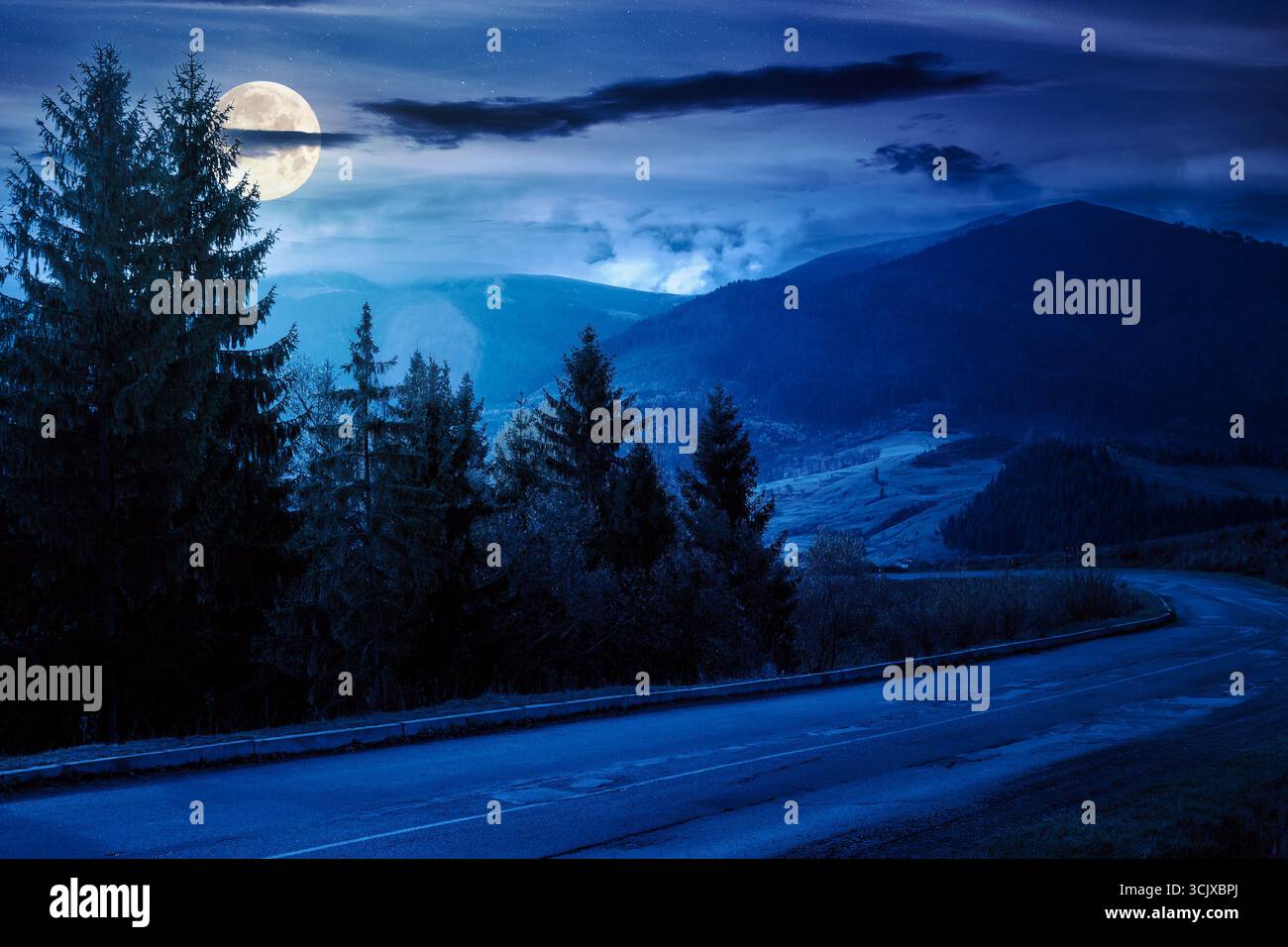 road through mountain landscape in autumn at night. countryside scenery in full moon light. spruce trees along asphalt paved pass in rustic area. trav Stock Photo