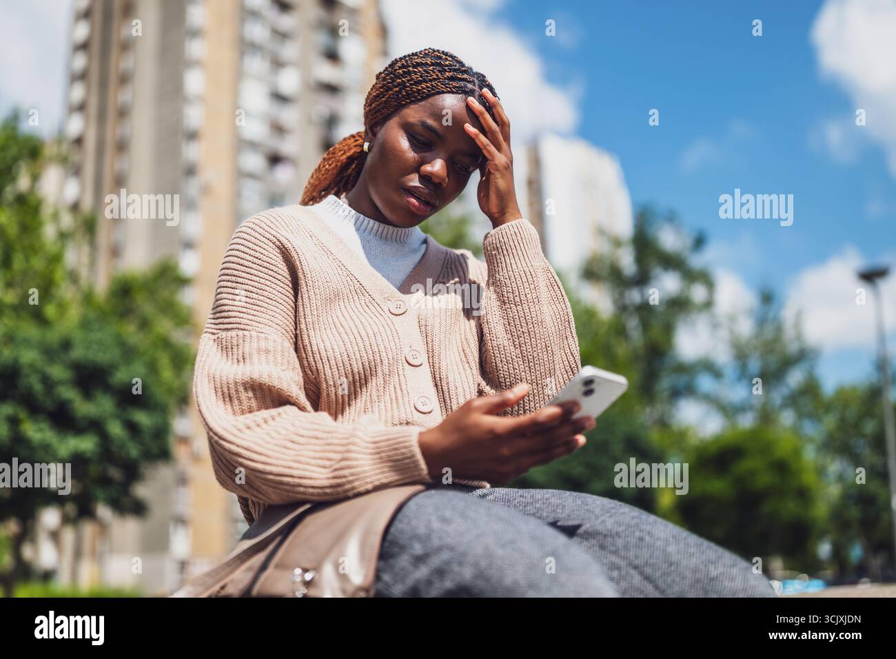 Young black woman is distraught while using smartphone for online messaging. Stock Photo