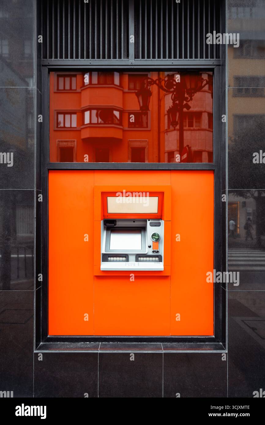 Modern ATM machine installed in a vibrant orange wall panel, with a ...