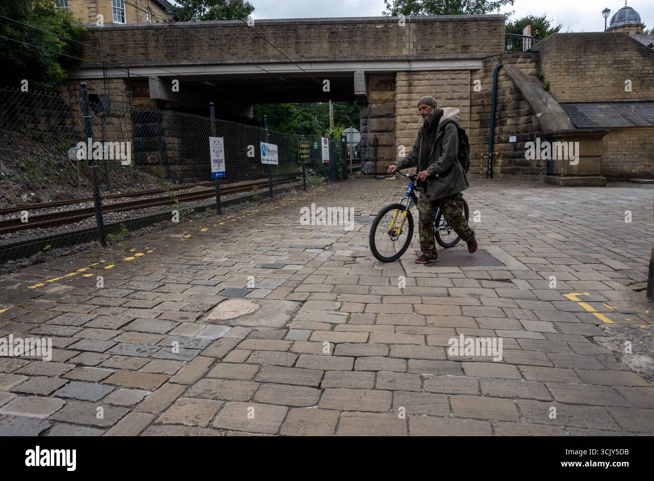 Man walks with bicycle past railway line at Saltaire, near Salts Mill, a historic Victorian industrial site in West Yorkshire, England Stock Photo