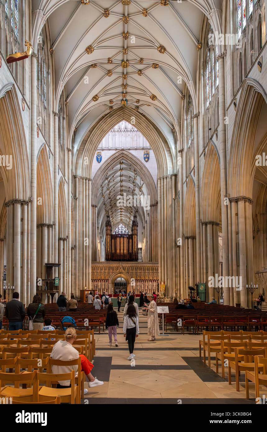 York Minster Cathedral interior in York, England, shows the central nave, altar, stained glass windows, ribbed vaults, pointed arches, and wooden pews Stock Photo
