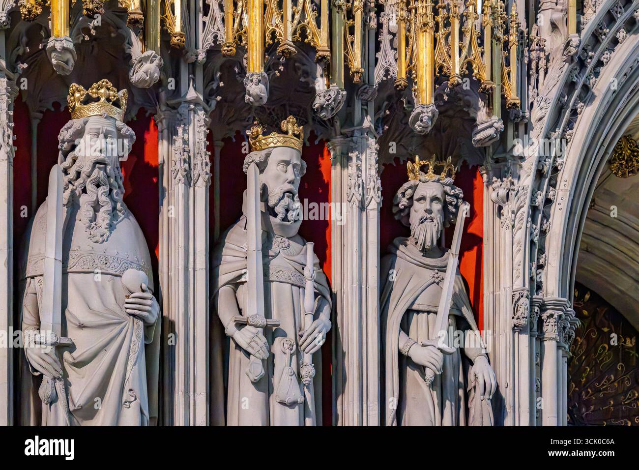 Three crowned stone figures in Gothic niches at York Minster, holding symbolic objects against a vivid red and gold architectural backdrop. Stock Photo