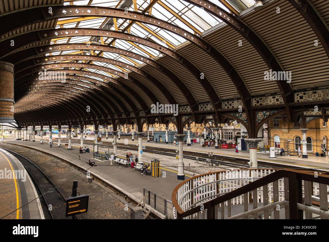 Passengers move through York railway station, beneath vaulted glass panels and ornate ironwork, as trains arrive and depart on multiple platforms Stock Photo