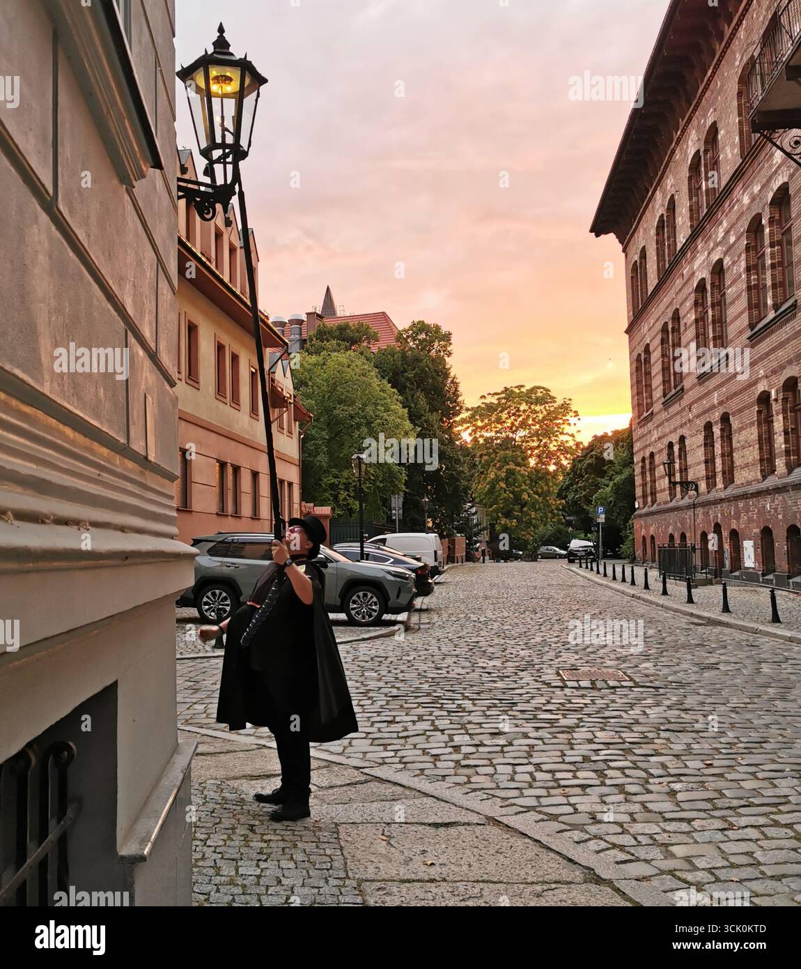 Wrocław lamplighter in hat and cloak lighting gas lamps on Cathedral Island at dusk—historic tradition, Poland, tourism, street scene, Ostrów Tumski. - Smartphone Captured Stock Image