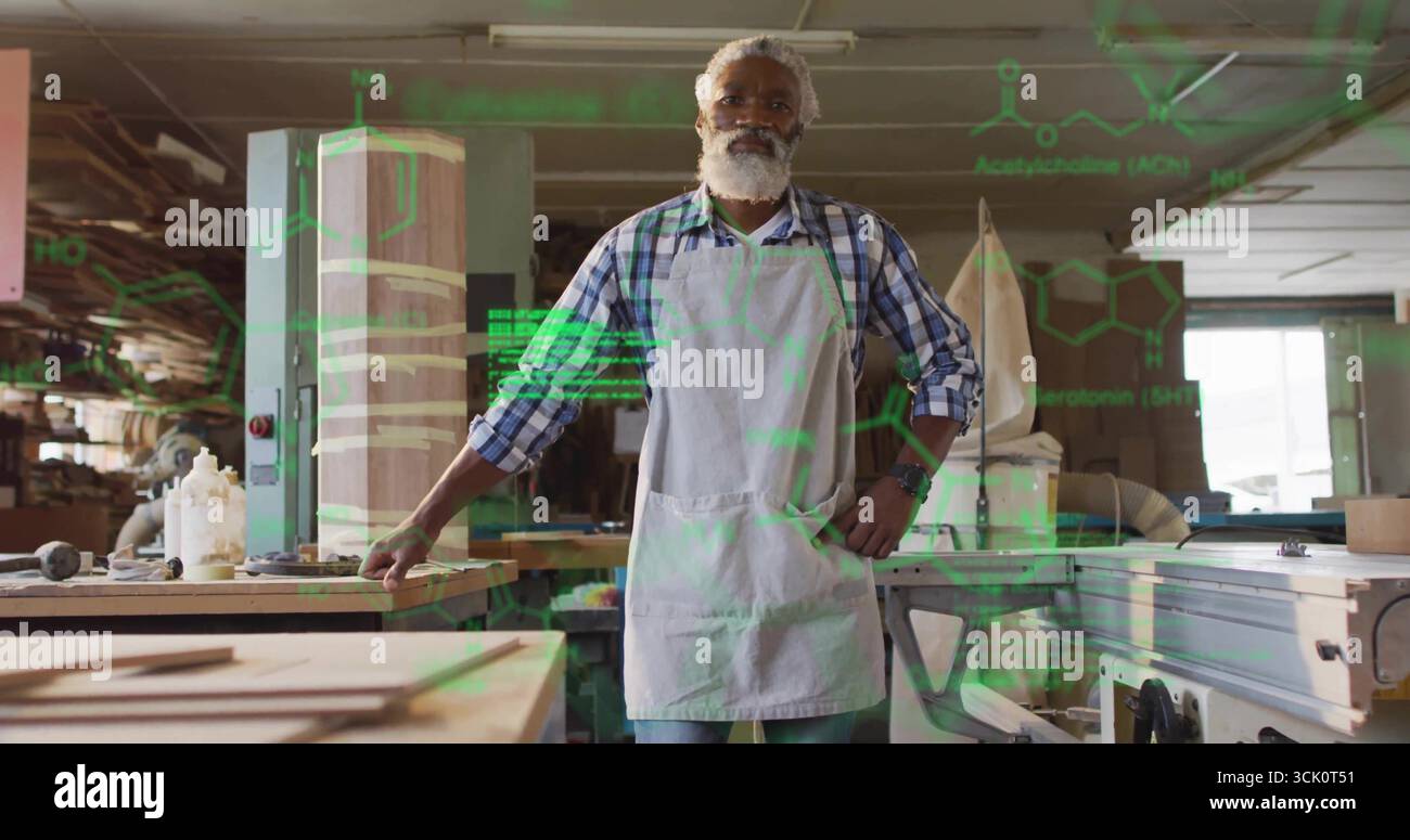 Standing African American carpenter in apron at workshop bench, with lumber, dust extraction hose Stock Photo