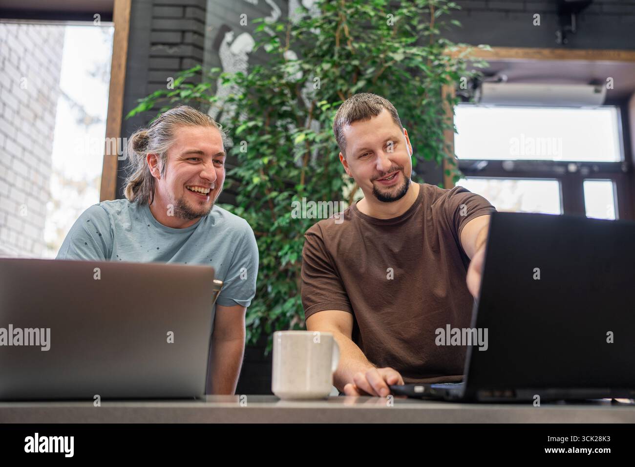 Two laughing It Software engineers working on project and programming in coffee shop. Successful start up project concept. Stock Photo
