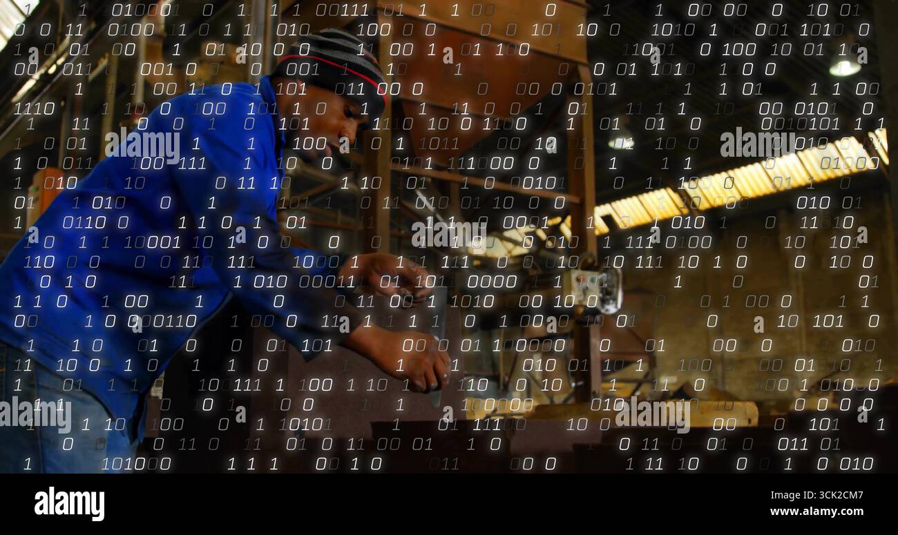 Operating machinist wearing ear protection adjusting lathe controls in workshop, binary overlay Stock Photo