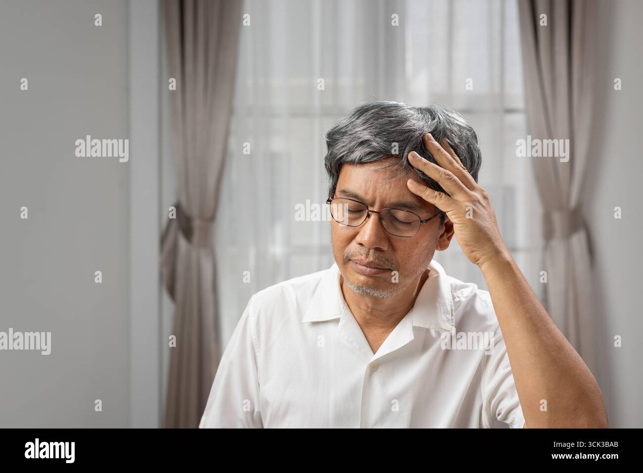 Senior asian man suffering from headache at home. Stock Photo