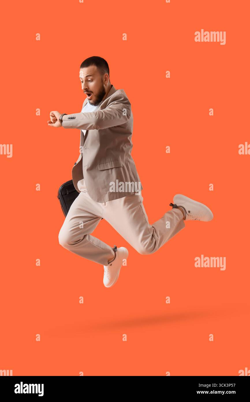 Surprised young businessman checking time while jumping on orange background Stock Photo