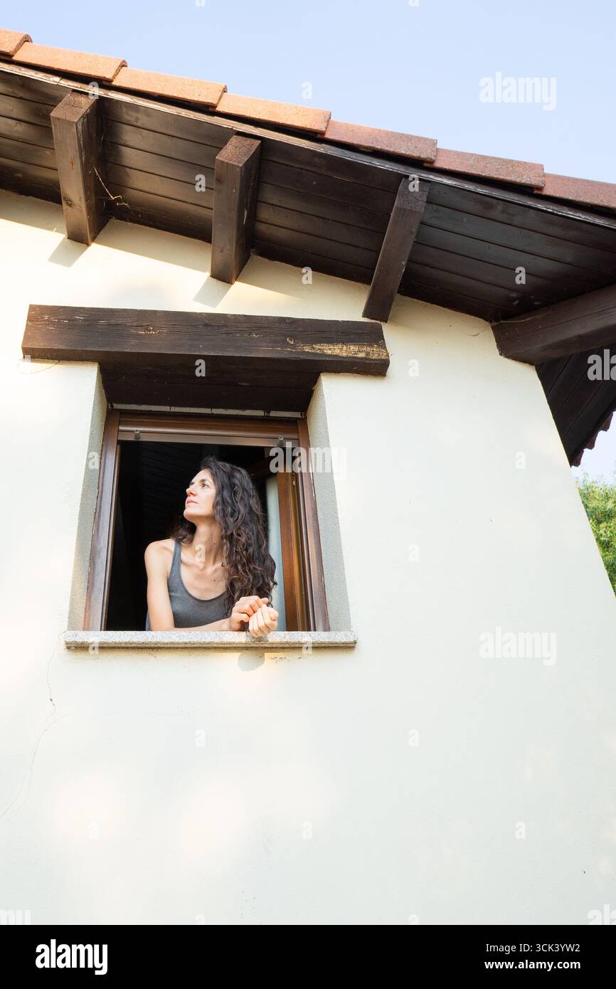 Serene woman enjoying fresh air while looking out the window of her cozy house Stock Photo