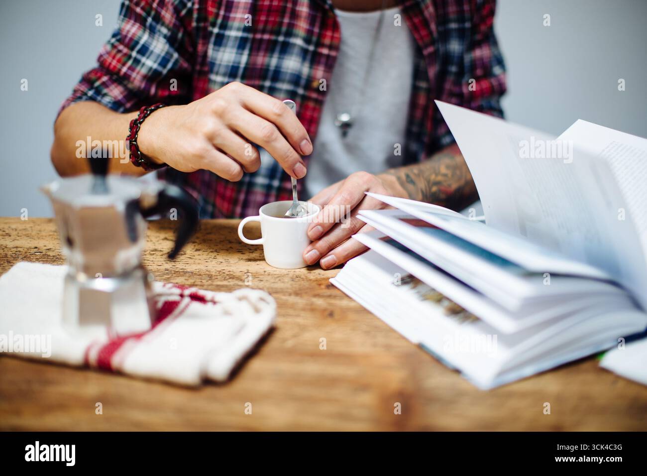 Young man stirring his coffee while reading a book Stock Photo