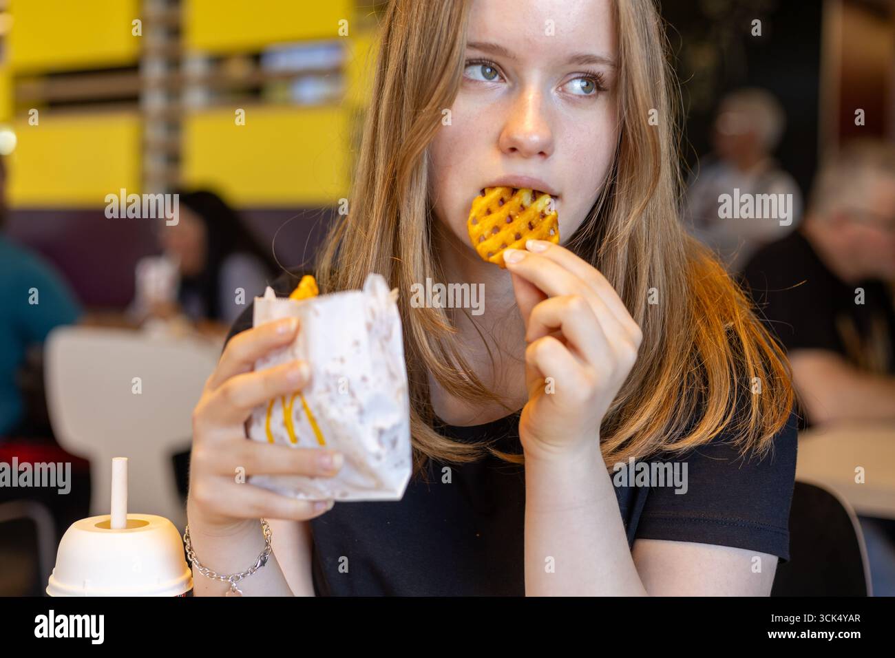 Kerpen, Germany - August, 9, 2025: Young woman eating waffle fries at McDonalds restaurant Stock Photo