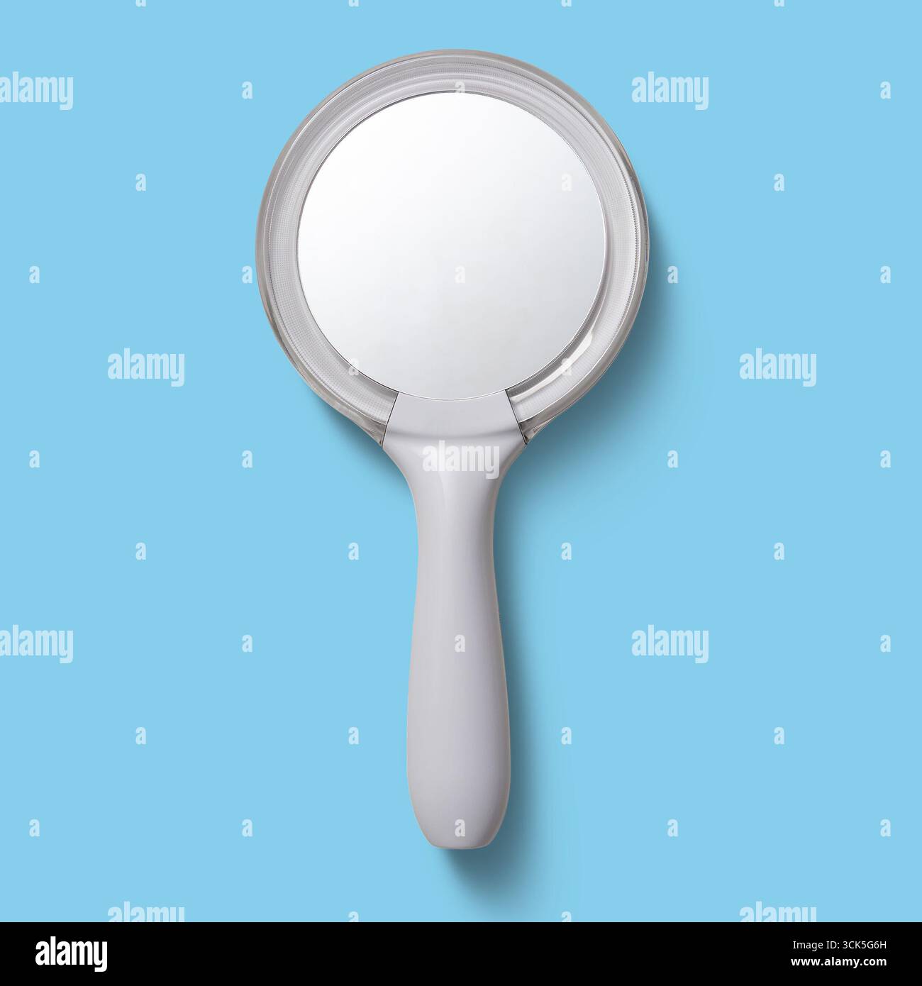 A handheld mirror with a round reflective surface and a simple white handle, used for personal grooming and reflection. Stock Photo