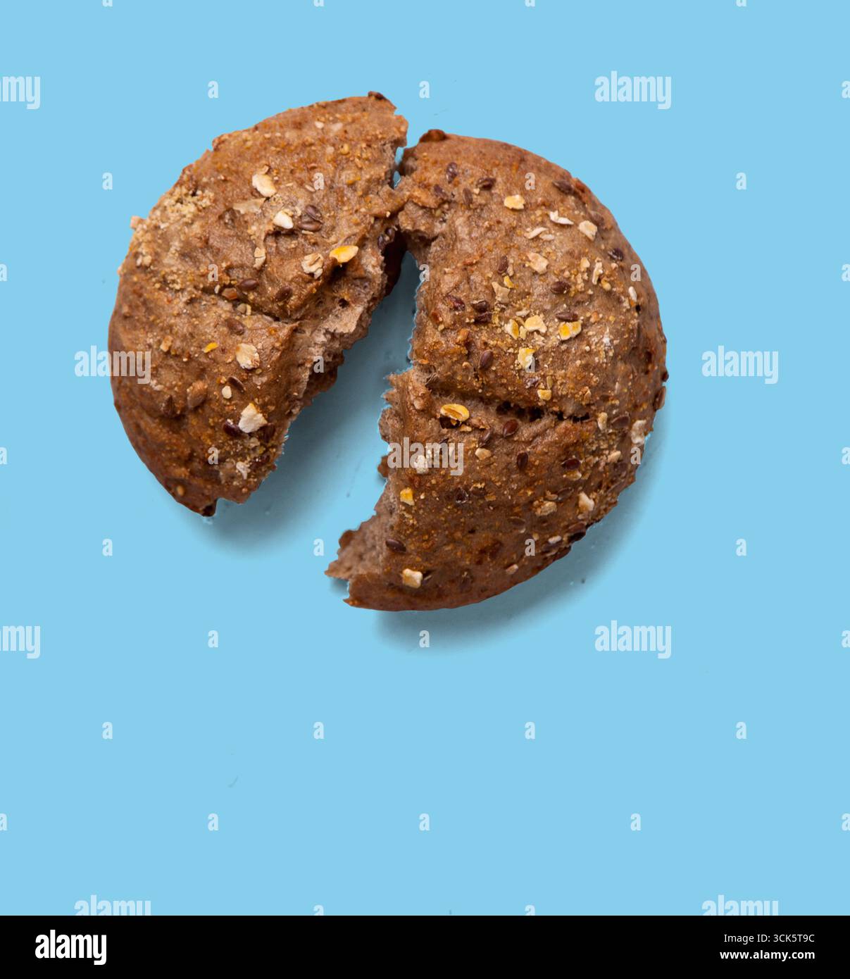 A broken round bread roll with visible grains and texture, highlighting its rustic appearance. Stock Photo
