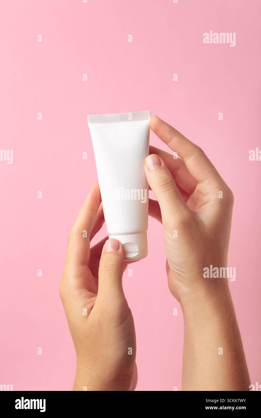 Hand holding blank white plastic tube on pink background. Top view ...
