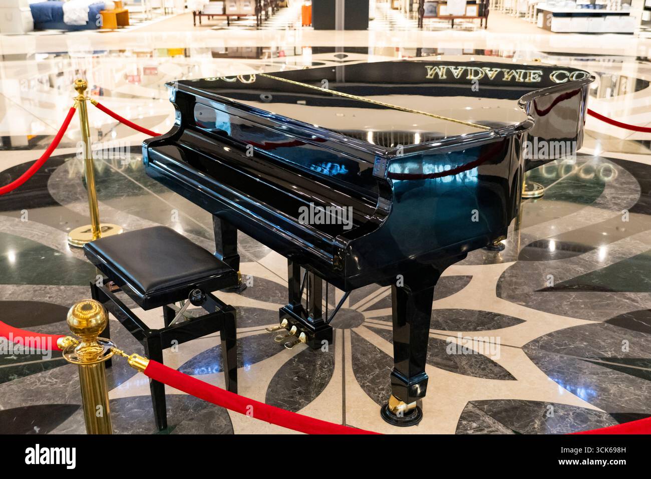 Glossy black grand piano with open lid, displayed in a luxurious public setting with marble floor and red velvet ropes Stock Photo