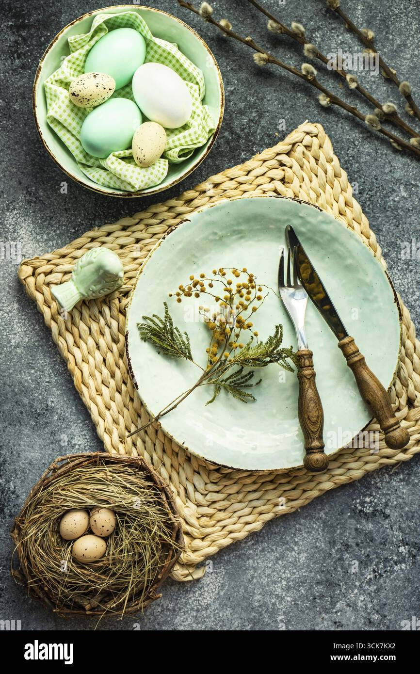 Festive holiday table setting for Easter dinner decorated with colored eggs on stone background with copy space Stock Photo