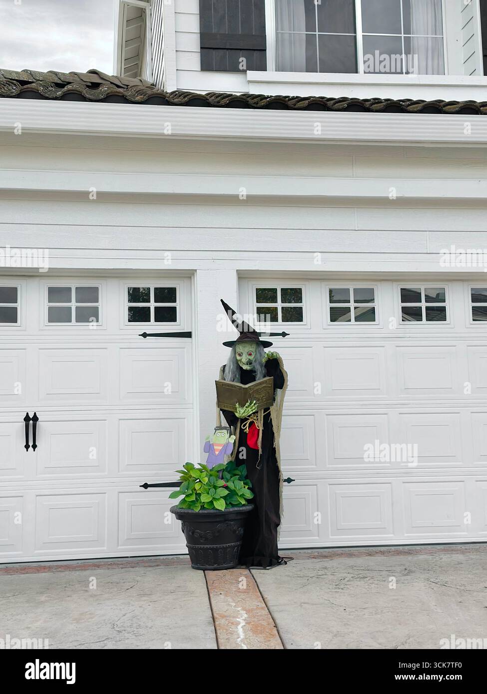 A witch figure holding a book displayed in front of a suburban garage as part of Halloween decorations. - Smartphone Captured Stock Image