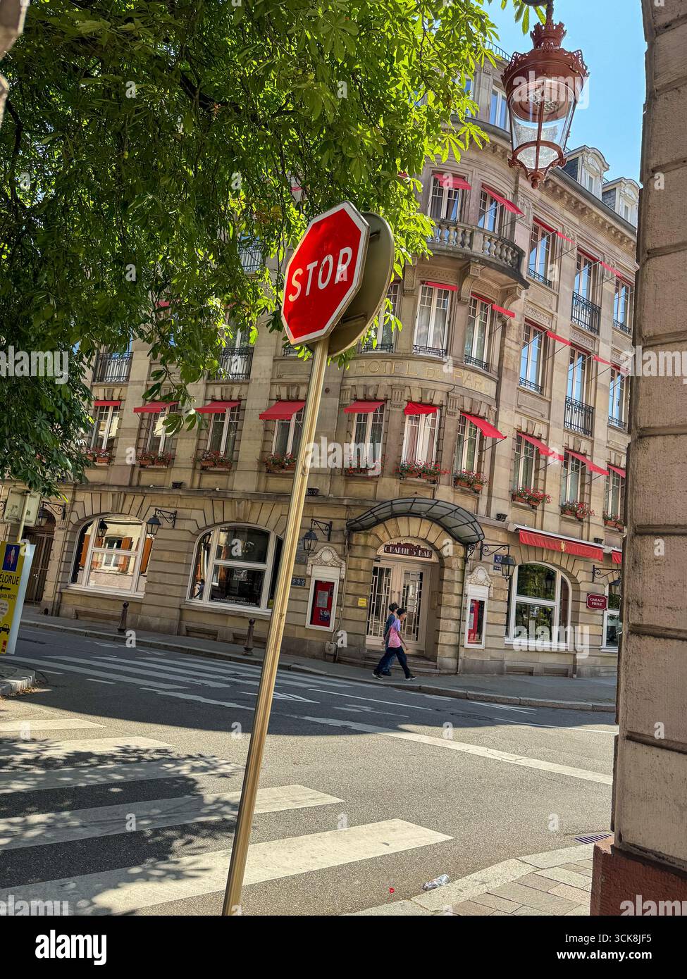French street with red stop sign, classic stone building, red awnings, wrought-iron balconies, and pedestrian at zebra crossing. - Smartphone Captured Stock Image French street with red stop sign, classic stone building, red awnings, wrought-iron balconies, and pedestrian at zebra crossing. - Smartphone Captured Stock Image