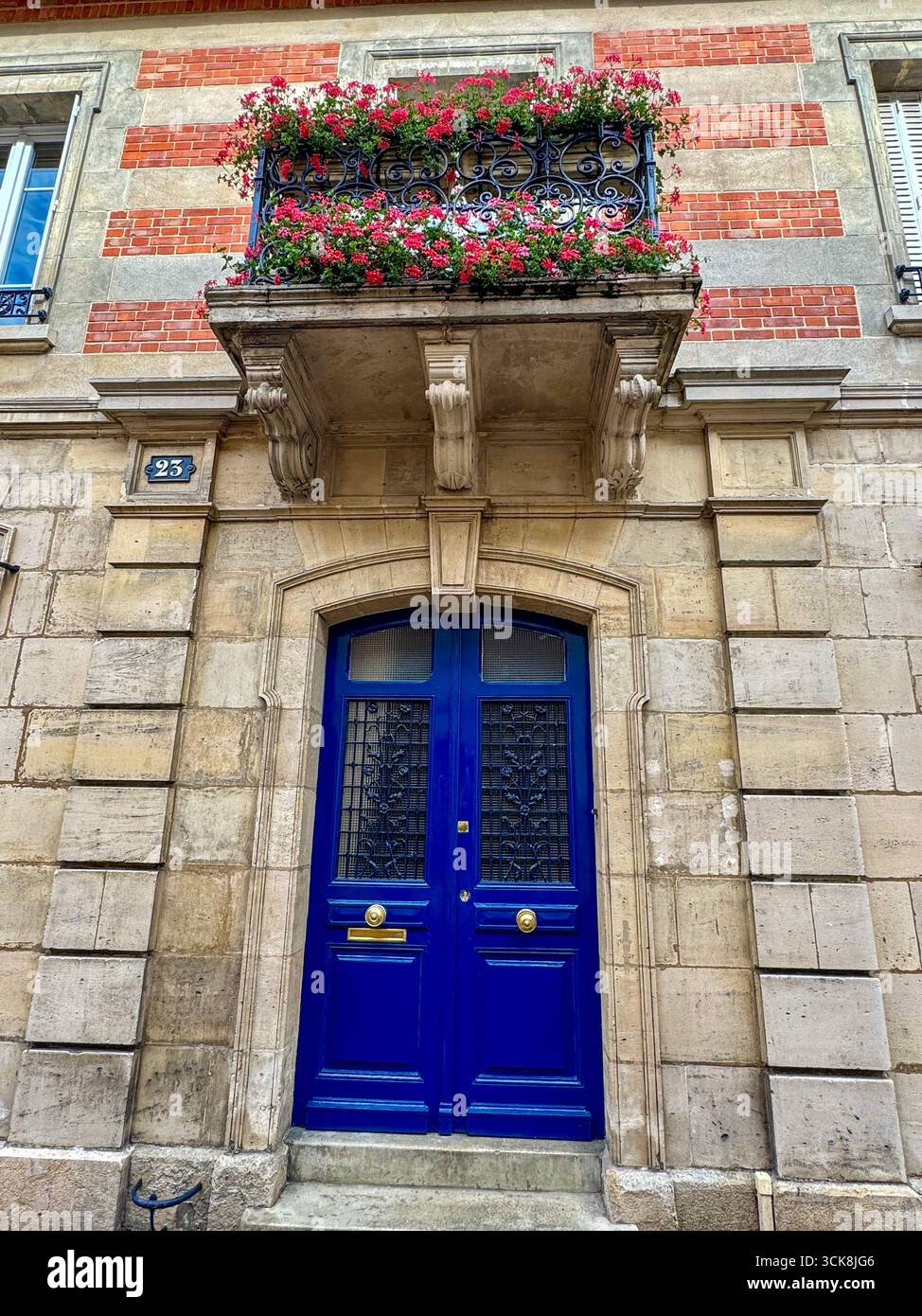 Elegant blue double door with wrought iron grilles, brass details, and flowerd balcony on stone and brick facade. - Smartphone Captured Stock Image