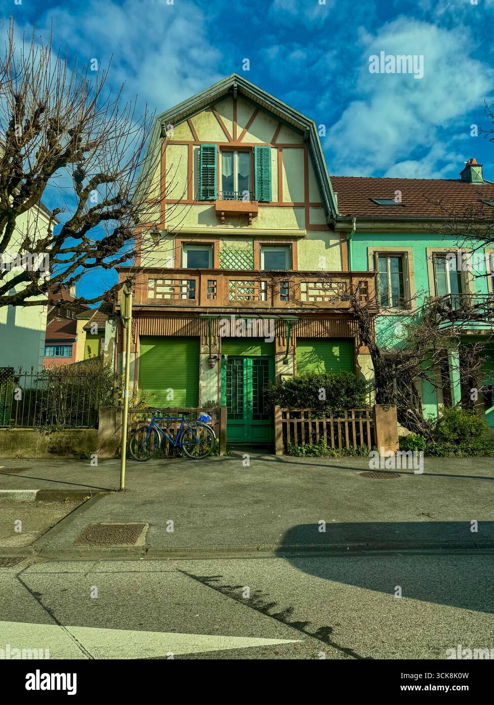 Traditional european residential house in Audincourt, France, with timber framing, green shutters, red tiled roof, and bicycles parked in frond. - Smartphone Captured Stock Image