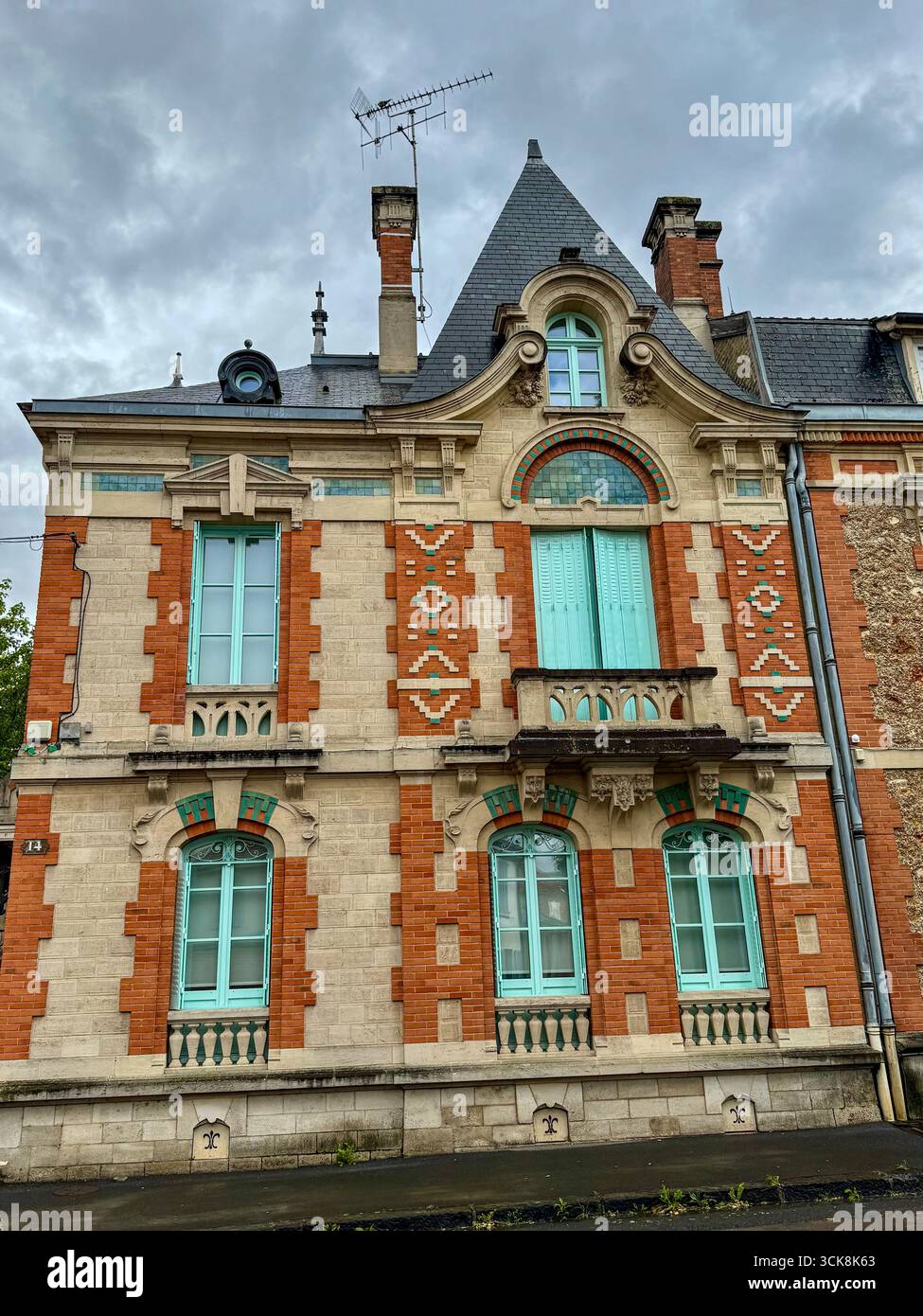 Elegant European historic facade with red brick, light stone, blue shutters, ornate carvings, and steep slate roof with dormer windows - Smartphone Captured Stock Image