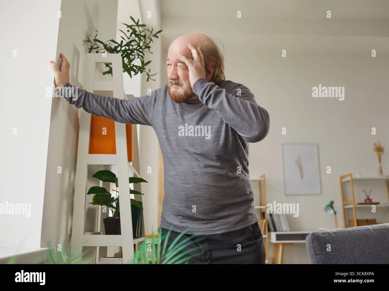 Dizzy senior man standing with hand on forehead, experiencing discomfort from vertigo or headache. Stock Photo