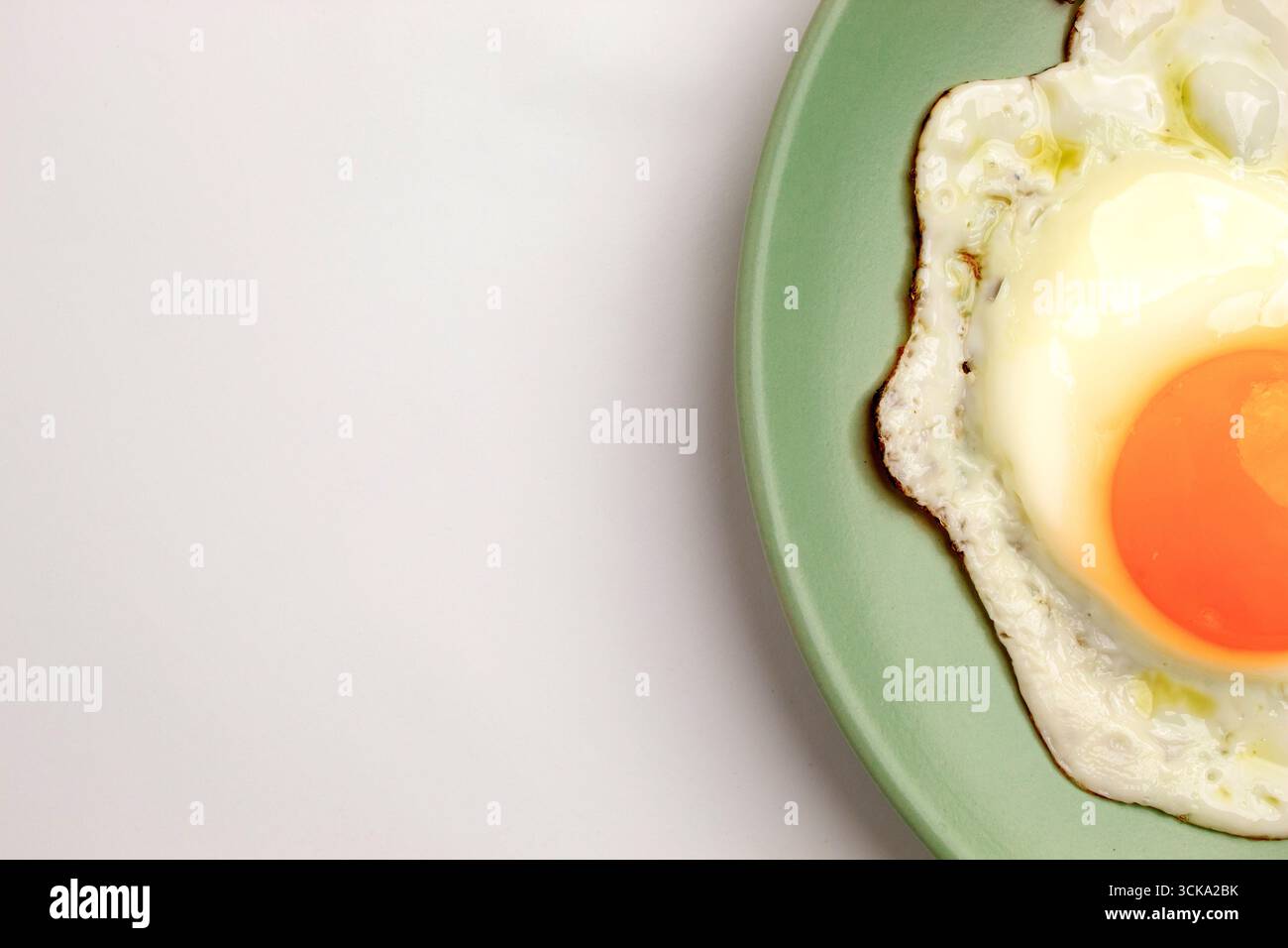 A fried egg on a pastel green plate on a pastel purple background. Close-up Stock Photo