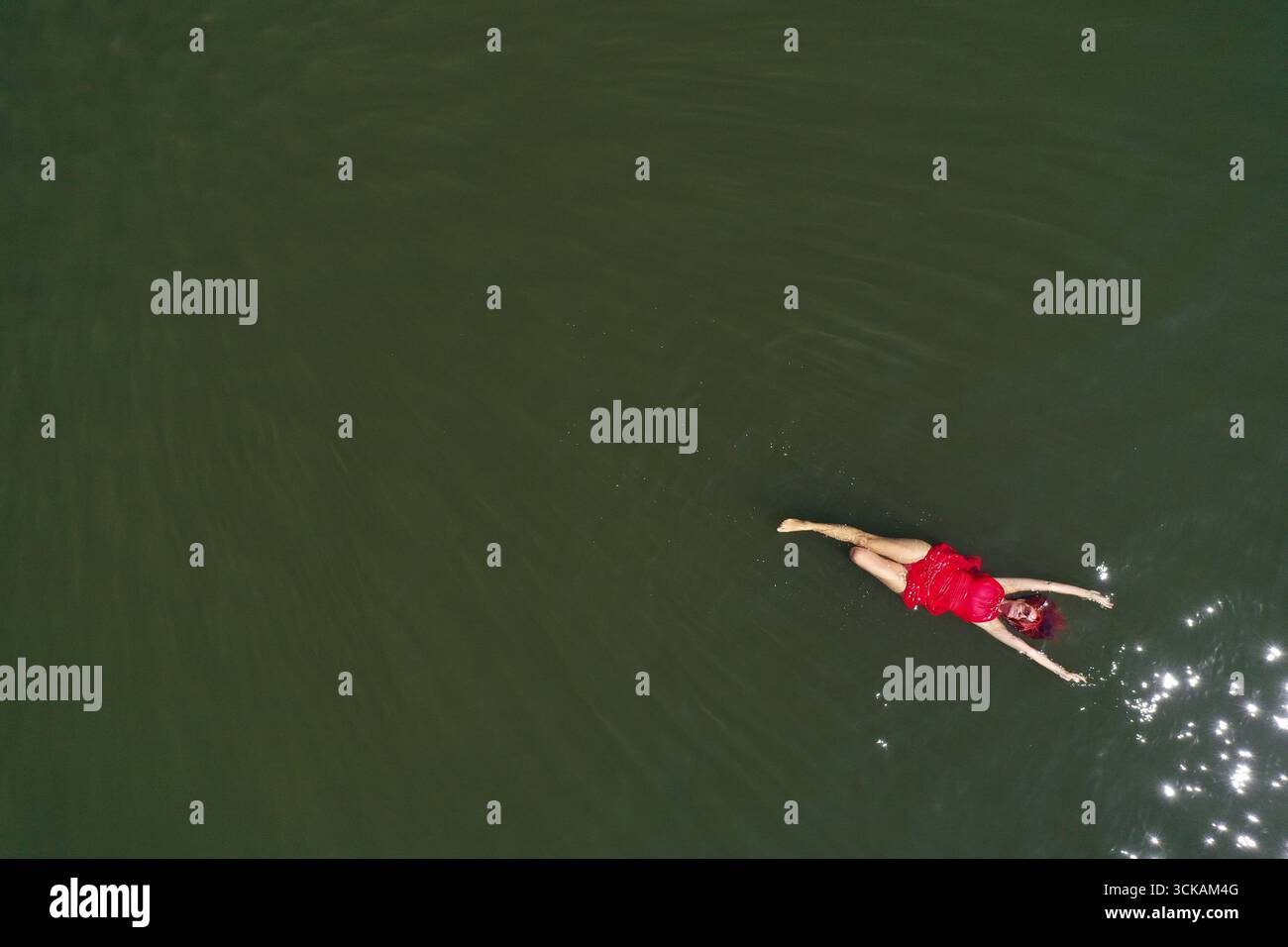Aerial view of a woman in a red dress swimming in a calm, dark body of ...