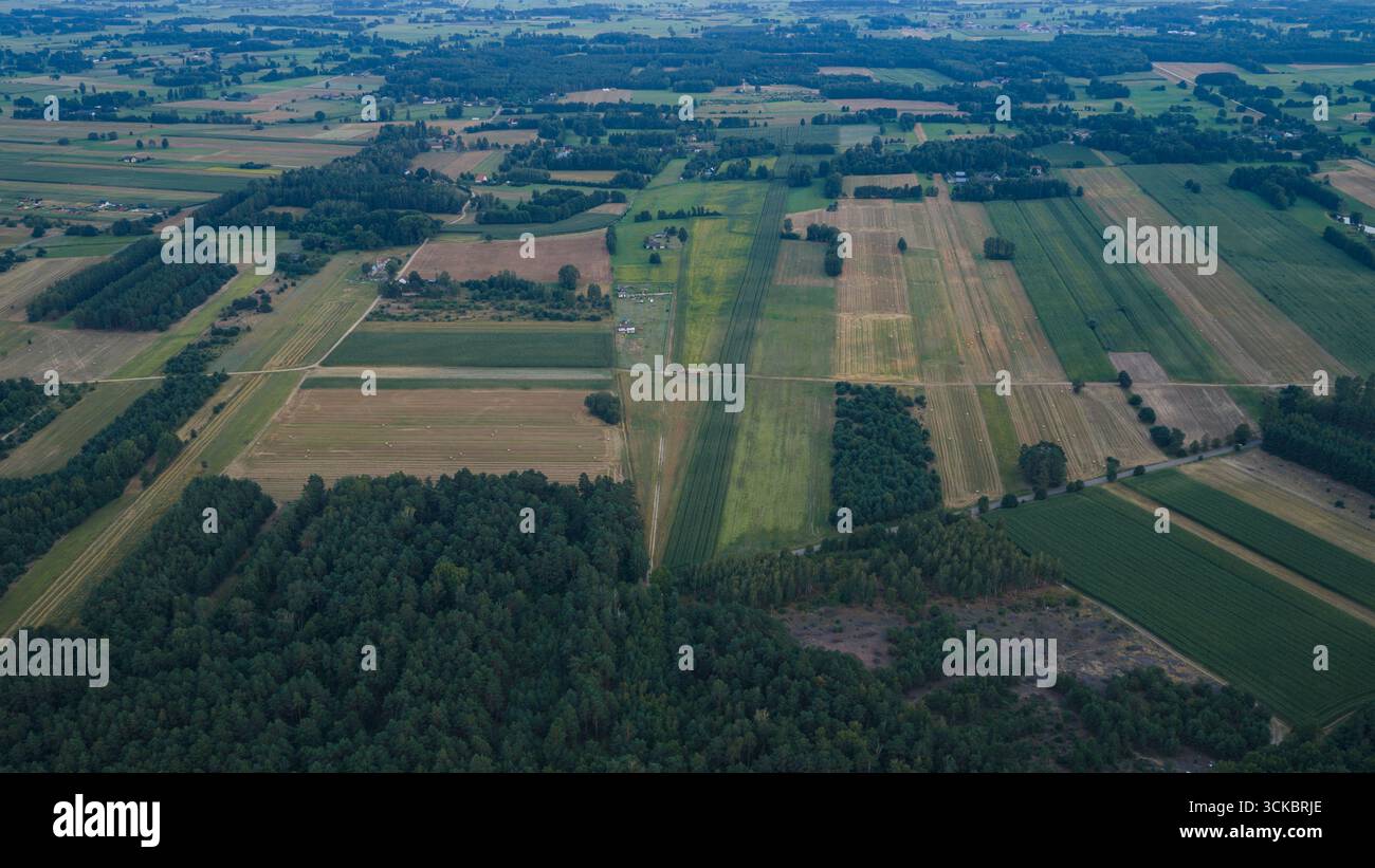 Bird's eye view of farmland near Nowy Lubiel, Poland, with fields in green and brown, scattered farmhouses, dirt roads, and dense forested areas. Stock Photo