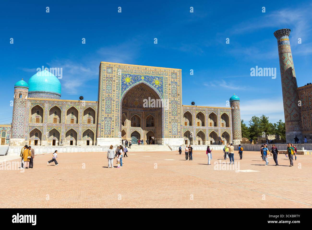 Samarkand, Uzbekistan - March 25, 2024: Tourists walk the Registan square on hot sunny day. Tilya-Kori Madrasah is on the background Stock Photo