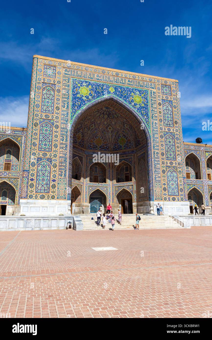 Samarkand, Uzbekistan - March 25, 2024: Vertical photo of Registan, tourists walk the square on a sunny day. Tilya-Kori Madrasah Stock Photo