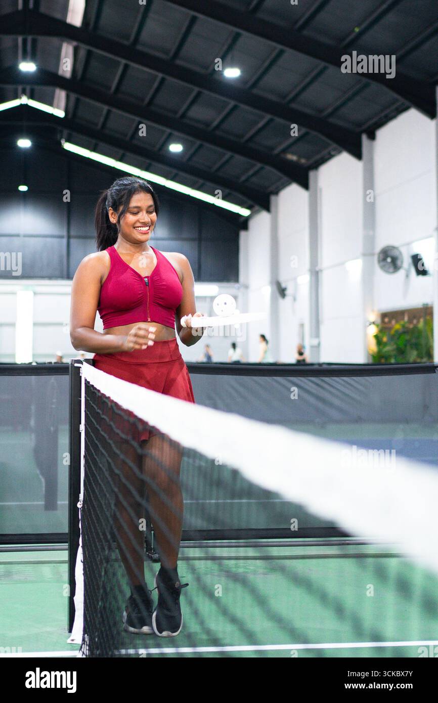 Young woman playing pickleball indoors, holding her paddle and smiling Stock Photo