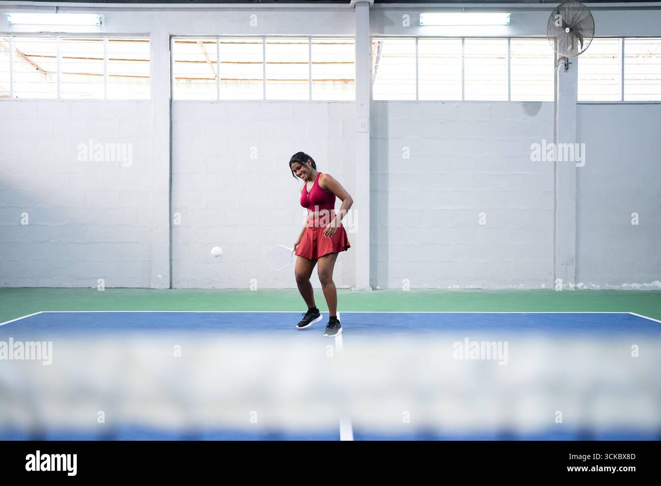 Young woman playing pickleball, serving the ball on an indoor court Stock Photo