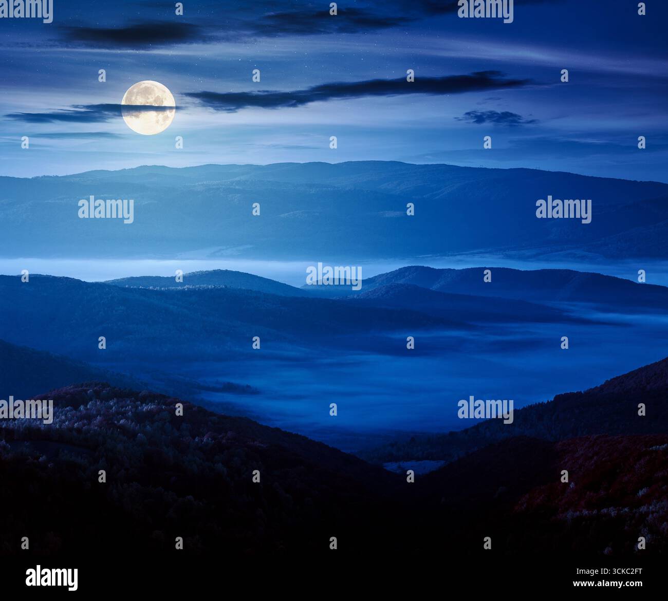 mountainous countryside landscape at night in autumn. trees in fall colors on rolling hills in full moon light. fog in distant valley. bright sky abov Stock Photo
