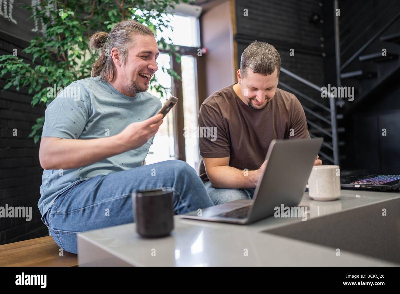 Two laughing It Software engineers working on project and programming in coffee shop. Successful start up project concept. Stock Photo