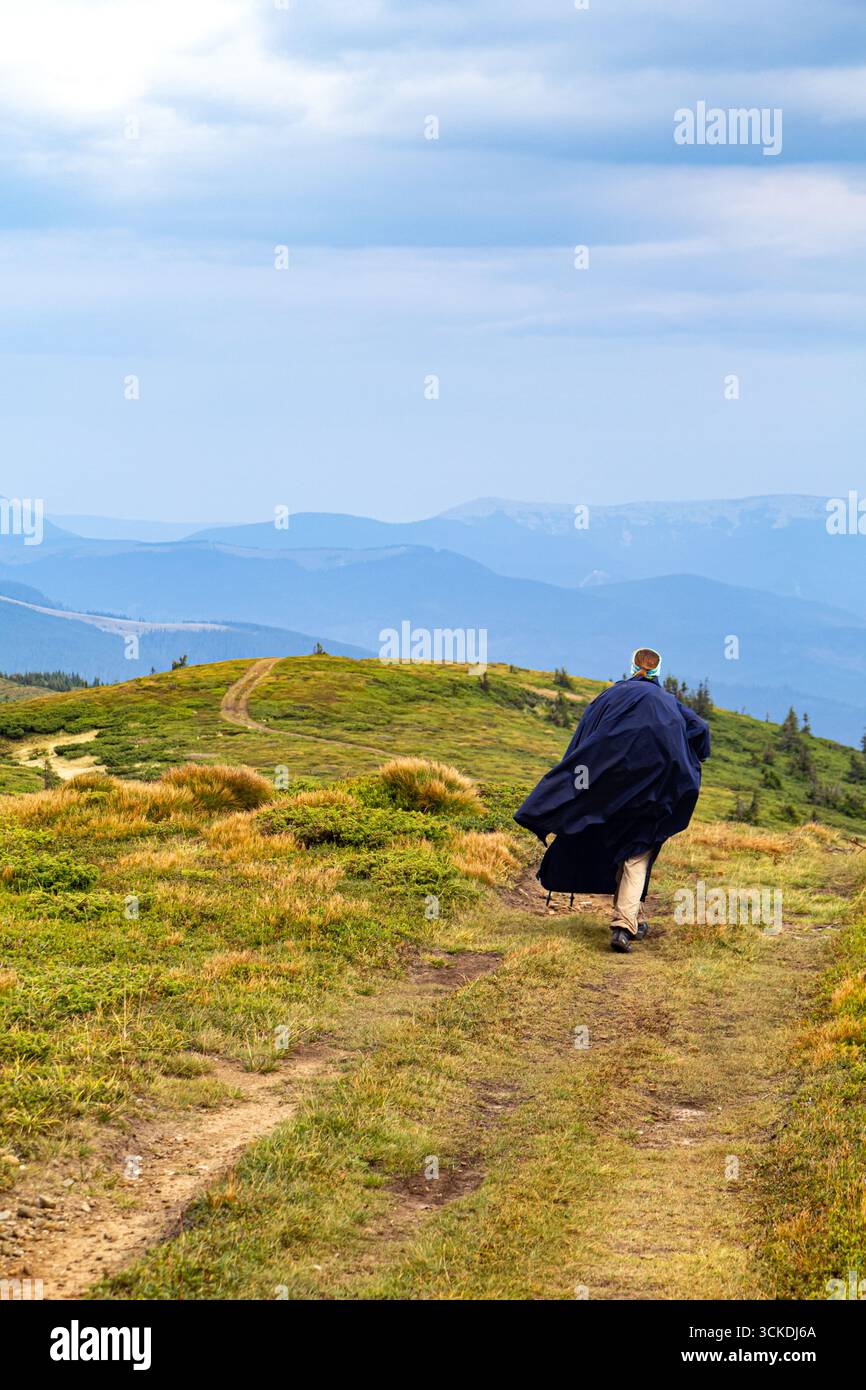 Vertical photo of a girl with backpack and raincoat hiking in the autumn mountains. Outdoor travel lifestyle and freedom. Stock Photo