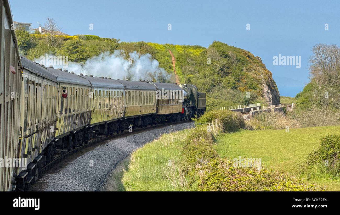 Paignton, Devon, England, UK - 24 April 2025: Steam engine pulling a train of vintage coaches through countryside on the Dartmouth Steam Railway. - Smartphone Captured Stock Image