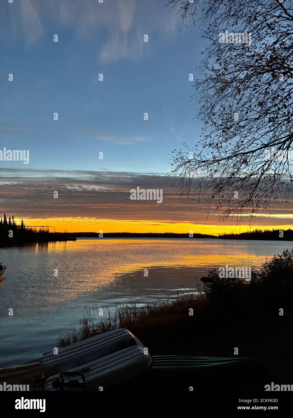 'Colorful sunset over a calm lake with boats at the shoreline and forest in the distance.' - Smartphone Captured Stock Image